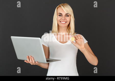 Freestyle. Femme debout isolé sur mur noir avec ordinateur portable montrant cryptocurrency coin smiling smiling Banque D'Images