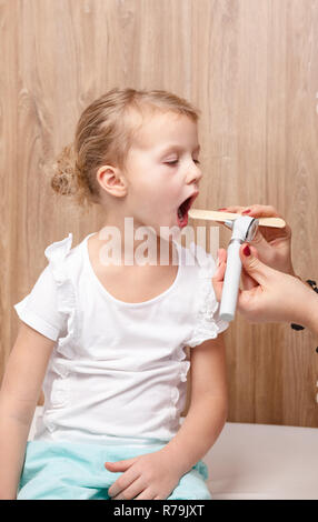 Femme pédiatre ou médecin examine la gorge de petite fille à l'aide d'abaisse-langue en bois et une lampe torche. L'examen physique de l'enfant conc Banque D'Images