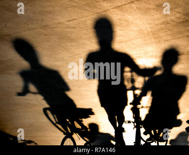 L'ombre floue de trois jeunes femmes à cheval ou en poussant leurs vélos dans le coucher du soleil Banque D'Images