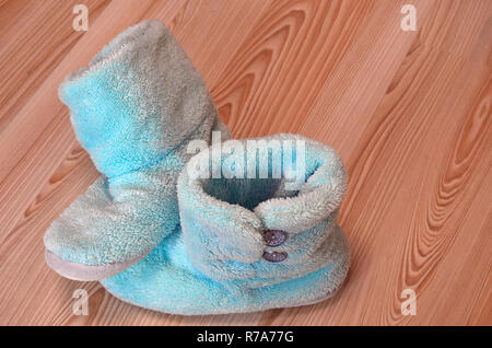 Chaussons bleu chaud en peluche debout sur un parquet en bois dans la chambre. Circuit de refroidissement d'hiver froid, réchauffement, house concept. Banque D'Images