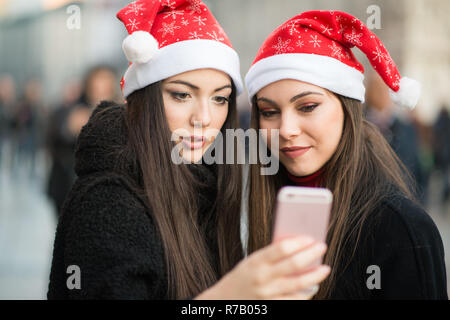 Smiling young women in Christmas hat en utilisant un smartphone ensemble Banque D'Images