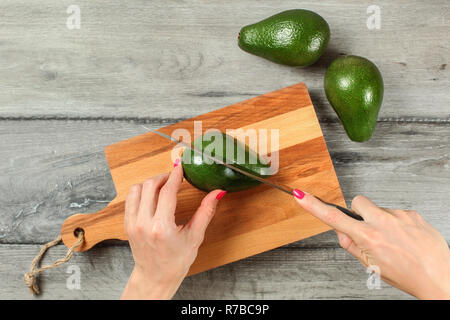 Vue sur table, femme mains tenant le couteau, couper l'avocat toute verte sur planche à découper. Banque D'Images