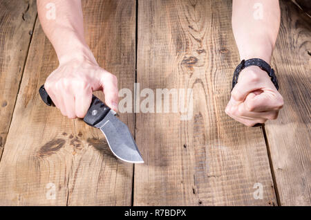 Grand couteau pliant dans la main. Mains et un couteau. Fond de bois. Banque D'Images