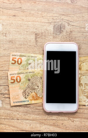 Billets de monnaie brésilienne : Reais. Le Brésil de l'argent. Vide de l'écran du smartphone et des projets sur la table en bois. Banque D'Images