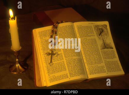 BIBLE SAINTE OUVERTE, CHAINES DE ROSAIRE AVEC UNE CROIX REPOSANT SUR UNE PAGE OUVERTE ET UNE BOUGIE BRÛLANT À CÔTÉ. Banque D'Images