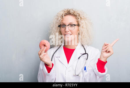 Jeune blonde dietist médecin femme de plus grunge grey wall eating très heureux pointant avec la main et le doigt sur le côté Banque D'Images