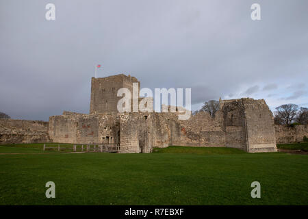 La garder à Portchester Castle dans le Hampshire en Angleterre. Ciels sombres derrière les murs en pierre. Union jack battant dans une forte brise Banque D'Images