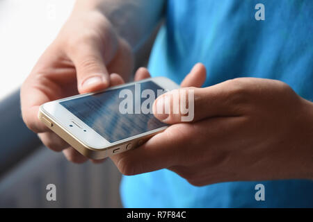 Teenage boy texting avec son iPhone d'Apple. Banque D'Images