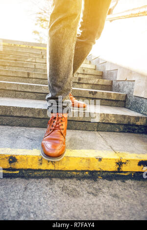 L'homme à de belles chaussures en cuir marron, marche le escaliers en granit dans un environnement urbain. Arrière-plan blanc. La vie au concept de mouvement Banque D'Images