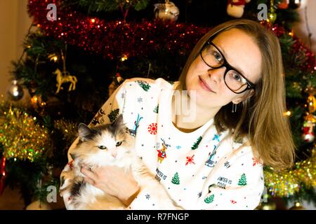 La veille de Noël et Nouvel an fille assise à l'arbre de Noël avec un chat dans ses mains. L'arbre est décoré en prévision de Noël Banque D'Images