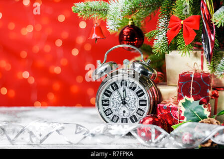 Vintage réveil à côté de cadeaux et décoration sur une planche en bois recouverte de neige sous un arbre de Noël sur fond brillant avec copie espace pour t Banque D'Images