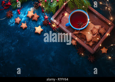 Cookies, thé et fairy lights mise à plat avec des branches de sapins, plateau en bois, étoile d'anis, et de décorations. Concept d'hiver chaud with copy space Banque D'Images