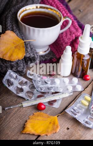 L'automne et les soins de santé. tasse de thé, pilules et thermomètre on a wooden background Banque D'Images