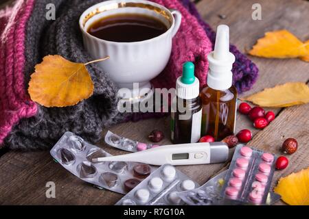 L'automne et les soins de santé. tasse de thé, pilules et thermomètre on a wooden background Banque D'Images