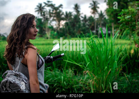 Une femme assise sur un vélo près d'un paysage fantastique, jungle, forêt tropicale en face d'elle et la nature.Concept de style, la mode dans l'aventure et les voyages avec accessoire python Banque D'Images