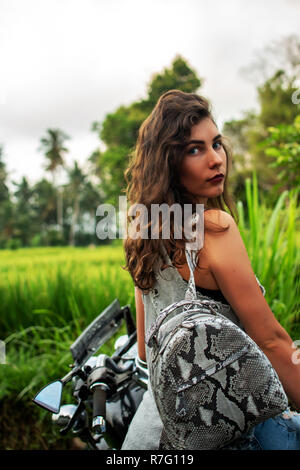 Une femme assise sur un vélo près d'un paysage fantastique, jungle, forêt tropicale en face d'elle et la nature.Concept de style, la mode dans l'aventure et les voyages avec accessoire python Banque D'Images