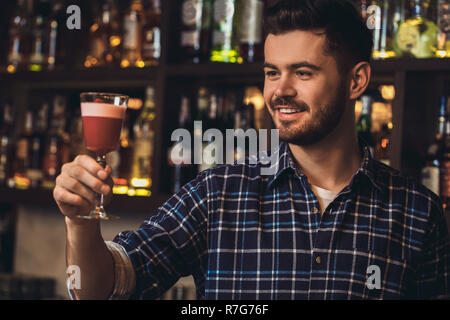 Jeune barman debout à comptoir bar à cocktail au sourire satisfait Banque D'Images
