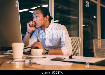 homme d'affaires assis dans le bureau travaillant sur ordinateur tard dans la nuit. Entrepreneur pensant pour la solution assis tard le soir dans le bureau. Banque D'Images