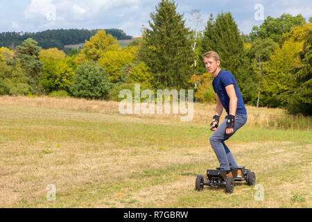 Young caucasian man rides mountainboard électrique off road dans la nature Banque D'Images