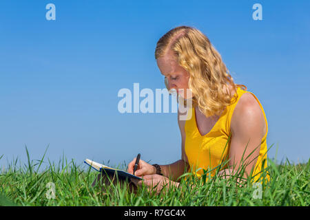 Young caucasian woman writing in grass with blue sky Banque D'Images