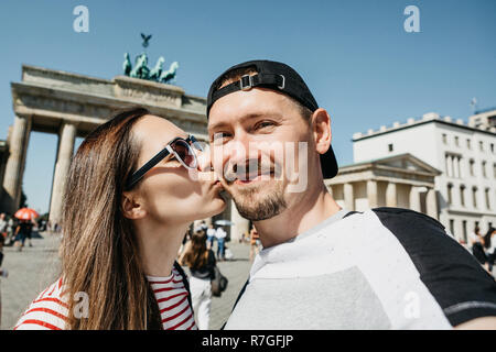 Belle jeune couple contre selfies l'arrière-plan de la porte de Brandebourg à Berlin en Allemagne. La jeune fille embrasse le gars. Banque D'Images