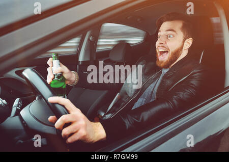Un homme ivre au volant d'une voiture avec une bouteille d'alcool dans sa main.Un homme est titulaire d'une roue motrice et une bouteille de bière. Banque D'Images