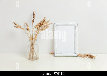 Maquette du châssis vertical avec seigle sauvage bouquet en vase en verre près de mur blanc. Cadre vide maquette pour sa présentation. Pour l'ossature du modèle ar moderne Banque D'Images