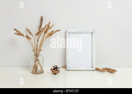 Maquette du châssis vertical avec seigle sauvage bouquet en vase en verre près de mur blanc. Cadre vide maquette pour sa présentation. Pour l'ossature du modèle ar moderne Banque D'Images