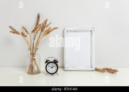 Maquette du châssis vertical avec seigle sauvage bouquet en vase en verre près de mur blanc. Cadre vide maquette pour sa présentation. Pour l'ossature du modèle ar moderne Banque D'Images