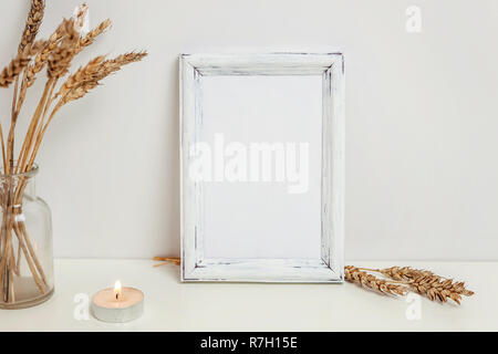 Maquette du châssis vertical avec seigle sauvage bouquet en vase en verre près de mur blanc. Cadre vide maquette pour sa présentation. Pour l'ossature du modèle ar moderne Banque D'Images