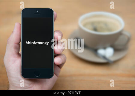 Un homme se penche sur son iPhone qui affiche le logo d'ThinkMoney (usage éditorial uniquement). Banque D'Images