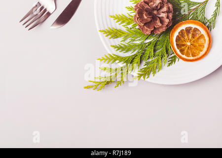 Plaque et décoré avec des couverts et des rameaux de conifères dry orange sur fond gris clair. Banque D'Images