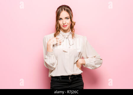 Une femme demande qui je suis, montrant sur eux-mêmes les doigts. Belle femelle portrait en pied isolé sur fond rose studio. Les jeunes surpris émotionnelle woman looking at camera.les émotions humaines, l'expression faciale concept Banque D'Images