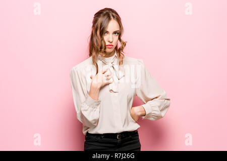 Une femme demande qui je suis, montrant sur eux-mêmes les doigts. Belle femelle portrait en pied isolé sur fond rose studio. Les jeunes surpris émotionnelle woman looking at camera.les émotions humaines, l'expression faciale concept Banque D'Images