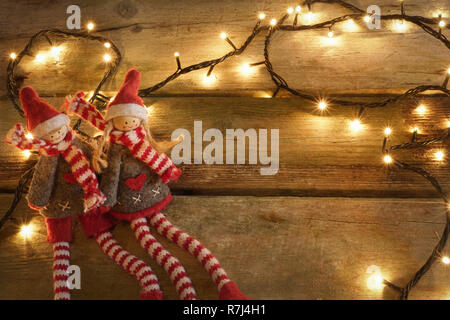 Paire de mignon et adorable lutins de Noël assis à table rustique en bois jaune avec des lumières de Noël. Avec l'exemplaire de l'espace. Banque D'Images