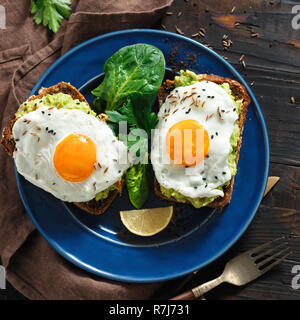 L'avocat des toasts avec des oeufs frits dans un joyeux visages sur table en bois sombre. Vue supérieure de la table du petit déjeuner sain concept Banque D'Images