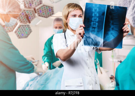 Femme médecin à à une radiographie de la colonne vertébrale. La chirurgie plus tourné l'arrière-plan. Banque D'Images