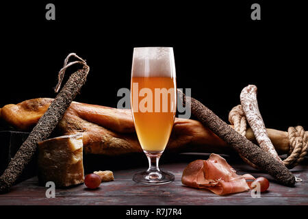 Un verre de bière légère mousse, jambe, jambon de Parme, cher variétés de saucisses et de fromage avec de la moisissure. Sur fond noir. Lieu de logo. Banque D'Images