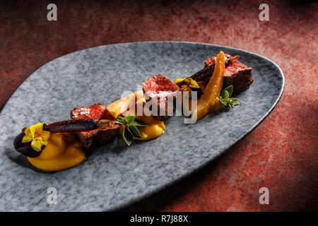 Filet de chevreuil avec purée de patate douce, carotte pourpre blanchies, confiture de coing avec du vin Banque D'Images