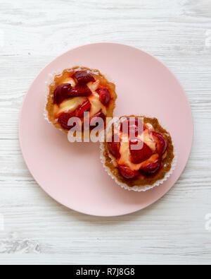 Fromage à la crème aux fraises tartelettes sur la plaque en bois blanc, rose sur la surface, les frais généraux. Close-up. Banque D'Images