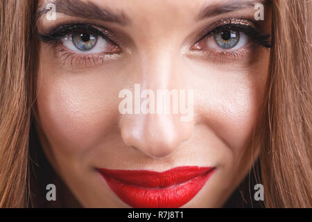 Portrait de femme aux cheveux long romantique attrayants avec des lèvres rouge portant robe noire debout sur l'arrière-plan gris Banque D'Images