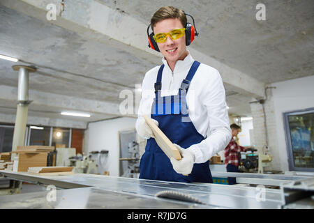Cheerful young carpenter avec planche en bois dans l'atelier Banque D'Images