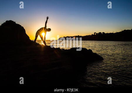 Argelès-sur-Mer (sud-est de la France). Quelqu'un pratique le yoga sur les rochers en face de la plage Racou au lever du soleil. Belle jeune femme avec de longues b Banque D'Images