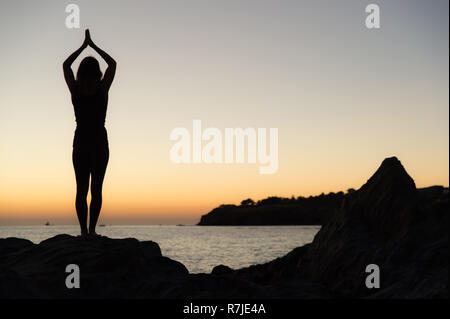 Argelès-sur-Mer (sud-est de la France). Quelqu'un pratique le yoga sur les rochers en face de la plage Racou au lever du soleil. Belle jeune femme avec de longues b Banque D'Images