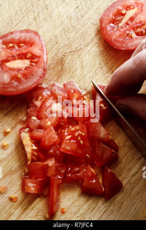 Coup de frais généraux de main tenant le couteau pour hacher et trancher juteux, tomates Salade red raw sur planche en bois. Banque D'Images