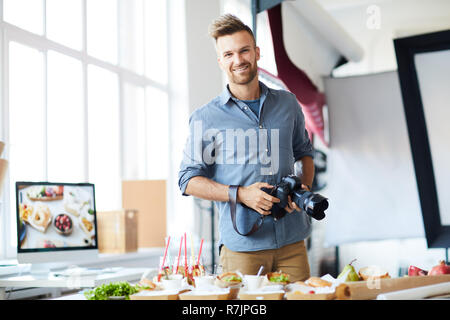 Waist up portrait of smiling at camera photographe tout en prenant des images de partie table dans Studio, copy space Banque D'Images