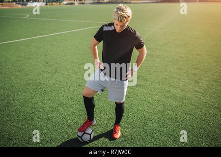 Jeune blonde player position sur pelouse et regarder vers le bas. Il pose. Guy Tenir les mains sur les hanches. Il est sur la pelouse. Soleil brille à l'extérieur. Banque D'Images