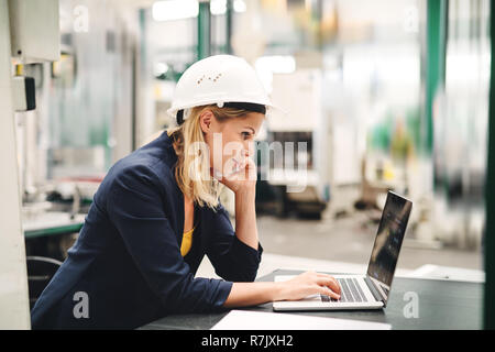Une femme ingénieur dans une usine à l'aide d'ordinateur portable et smartphone. Banque D'Images