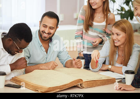 Les jeunes multiethniques sitting at table lecture Livres de référence pour l'étude des notes. Groupe de jeunes étudiants de l'école faire cession de bibliothèque. Banque D'Images