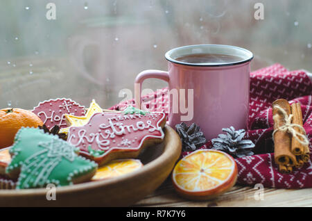 Une tasse de thé chaud se dresse sur une table en bois à côté d'une plaque de bois sur laquelle sont gingerbread cookies fabriqués à partir de tranches d'orange sur le fond d'une fenêtre avec des gouttes d'eau Banque D'Images